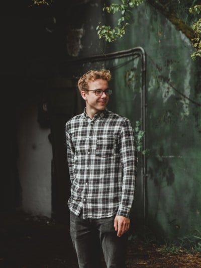 Dressed in blue and white plaid shirt man standing in the green wall
